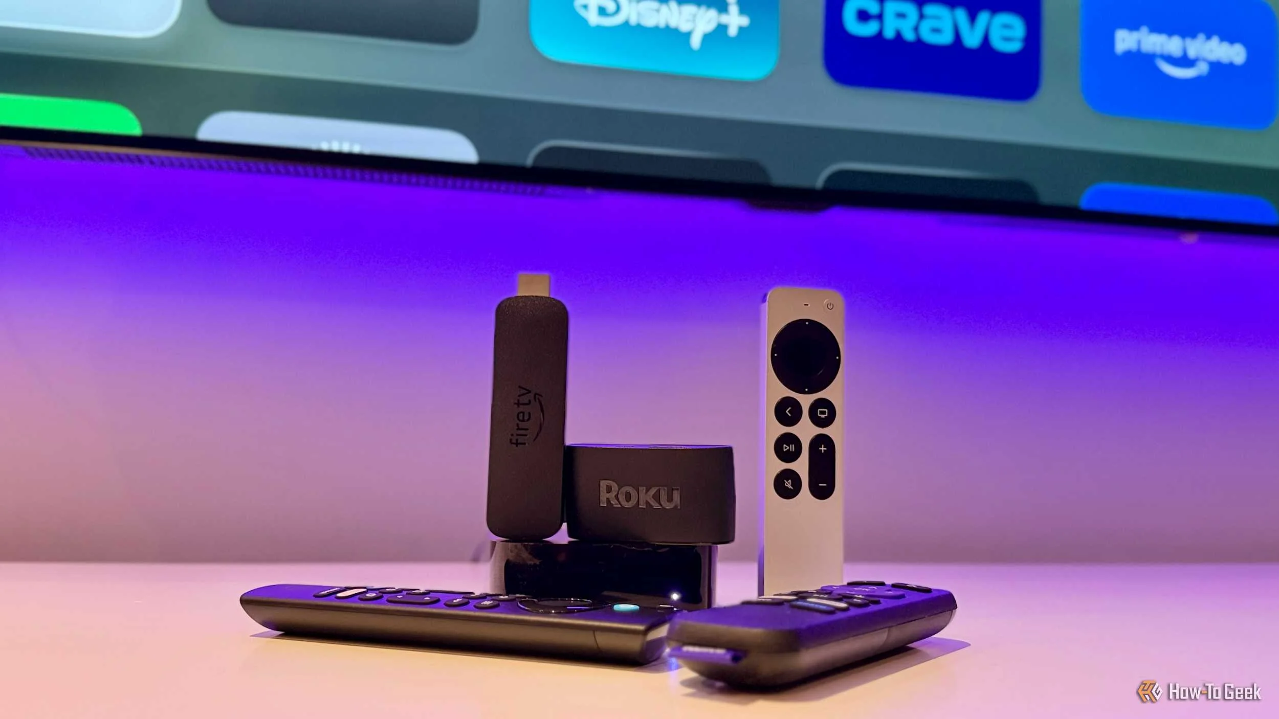 An Apple TV 4K, Fire TV Stick, and a Roku streaming device with their remotes