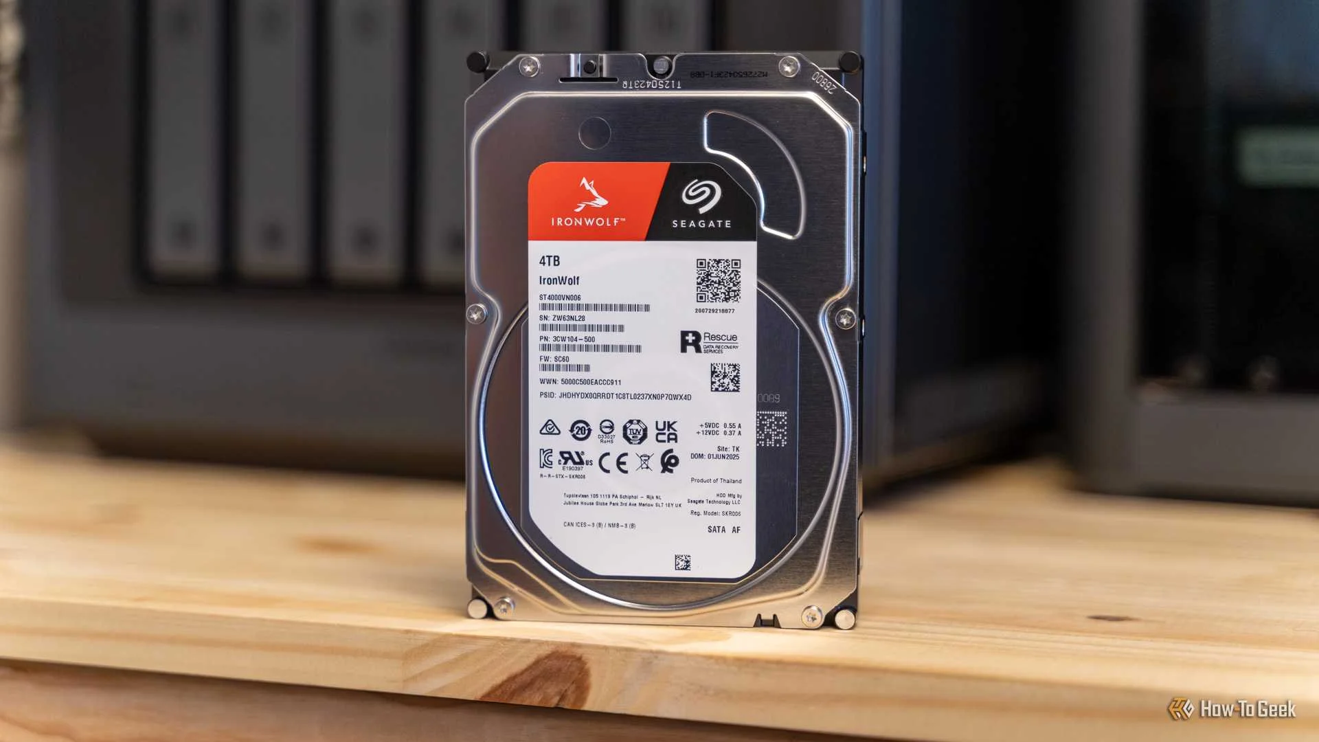 A Seagate IronWolf 4TB hard drive on a desk with the Ugreen iDX6011 Pro NAS slightly out of focus behind it.